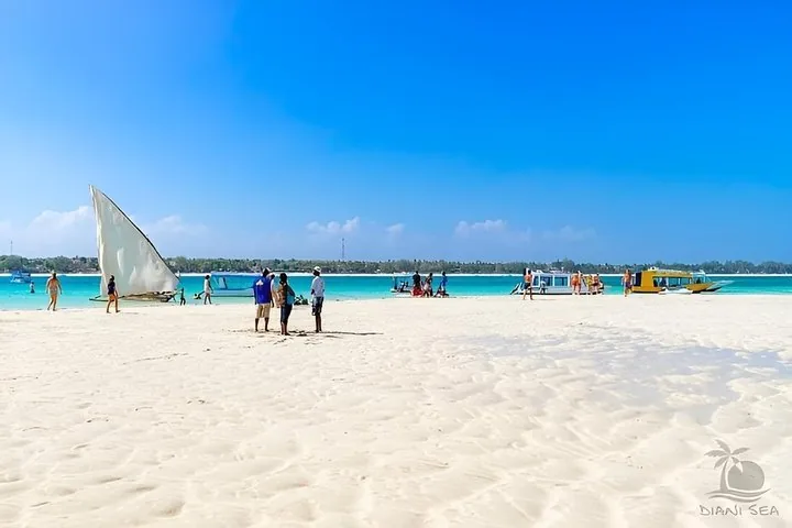 White sand beach meeting bright blue water with dhow and boats